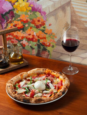 A burrata-topped pizza beside a glass of wine