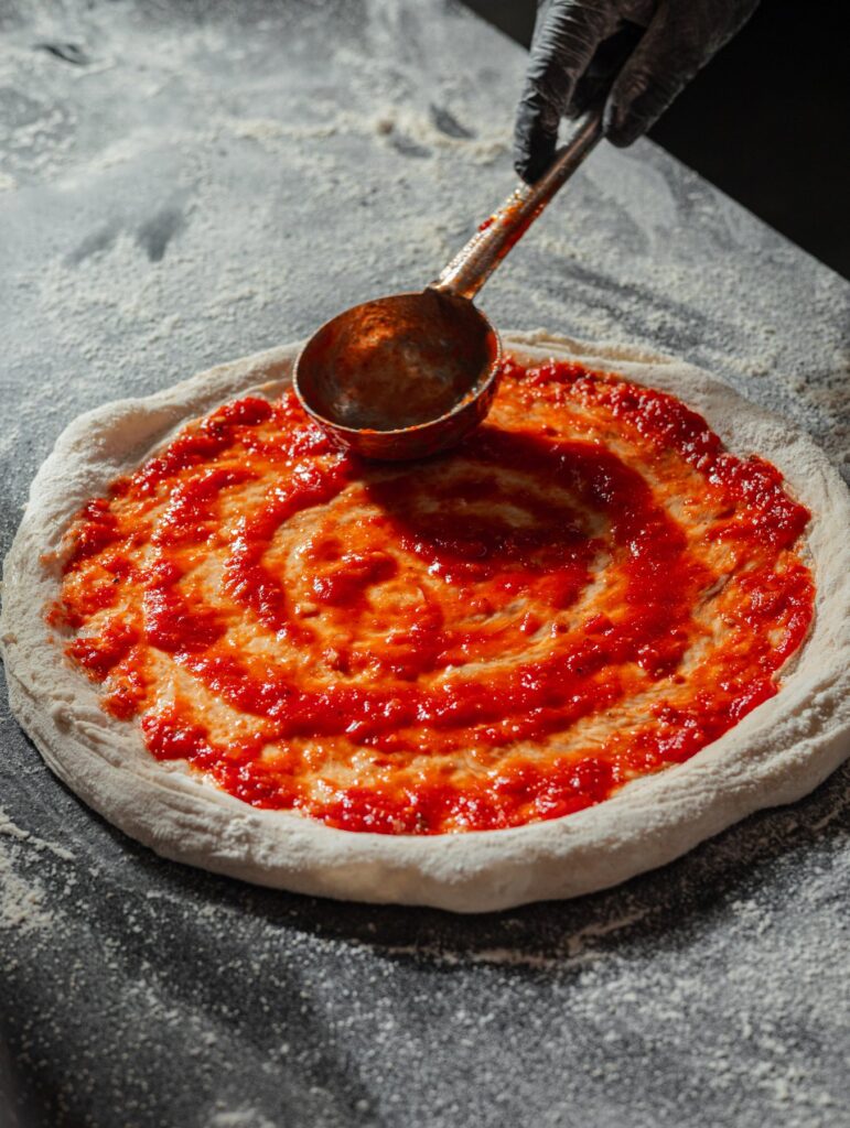 San Marzano tomato sauce being ladled onto a fresh dough base