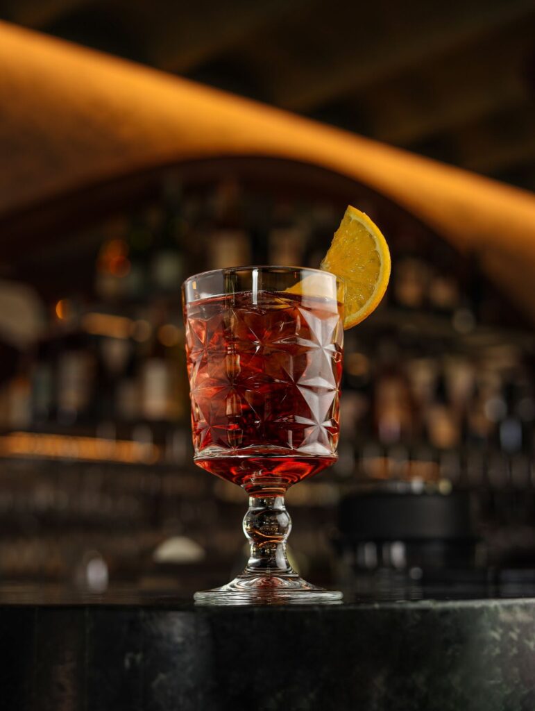 A red cocktail with a lemon twist at the bar